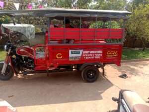 A bright red passenger motorized tuk-tuk vehicle with a canopy roof, featuring a side sign that reads 'Buggy Adventures Pick-Ups + Tours + Sunset Ride' parked on a paved driveway.