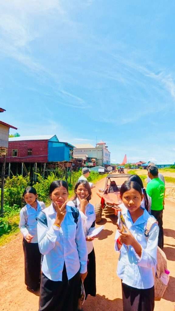 Cambodian schoolgirls in white uniforms smiling and posing on a dirt road in a stilt-house village during a countryside buggy tour stop near Siem Reap.